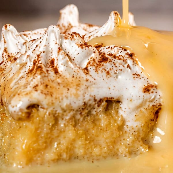Close-up of a toasted dessert topped with whipped cream, cinnamon, and warm caramel sauce dripping over the sides.