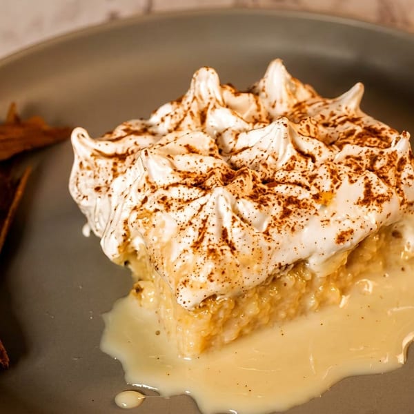 Slice of creamy cinnamon-spiced dessert topped with toasted meringue, plated with cinnamon sticks and sauce.